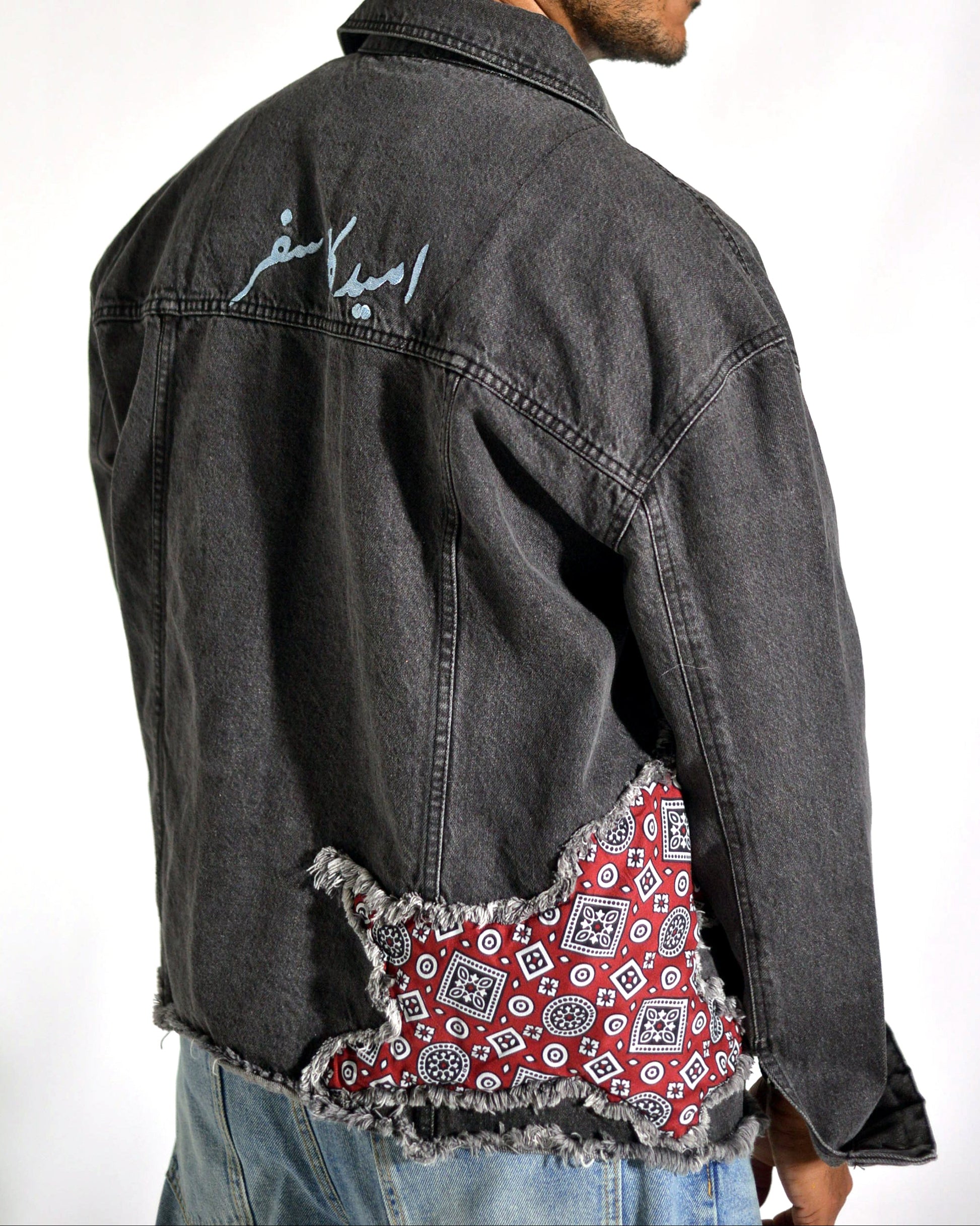 Man wearing a black denim jacket with a red and white patterned patch on the back, against a white background.