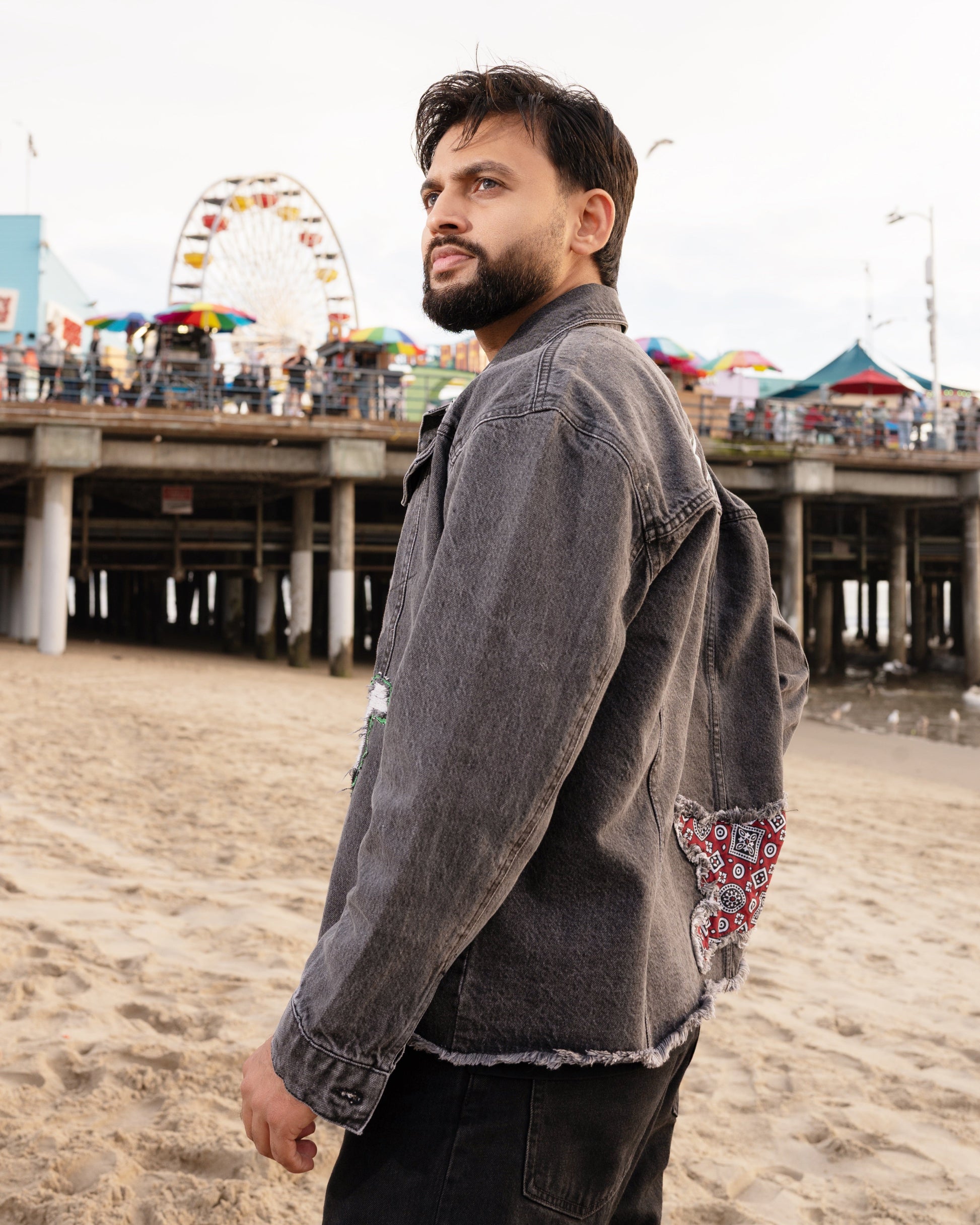 Man standing on a beach with a Ferris wheel and boardwalk in the background